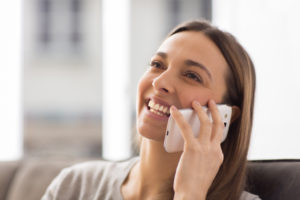 Pretty young female using white mobile phone at home smiling